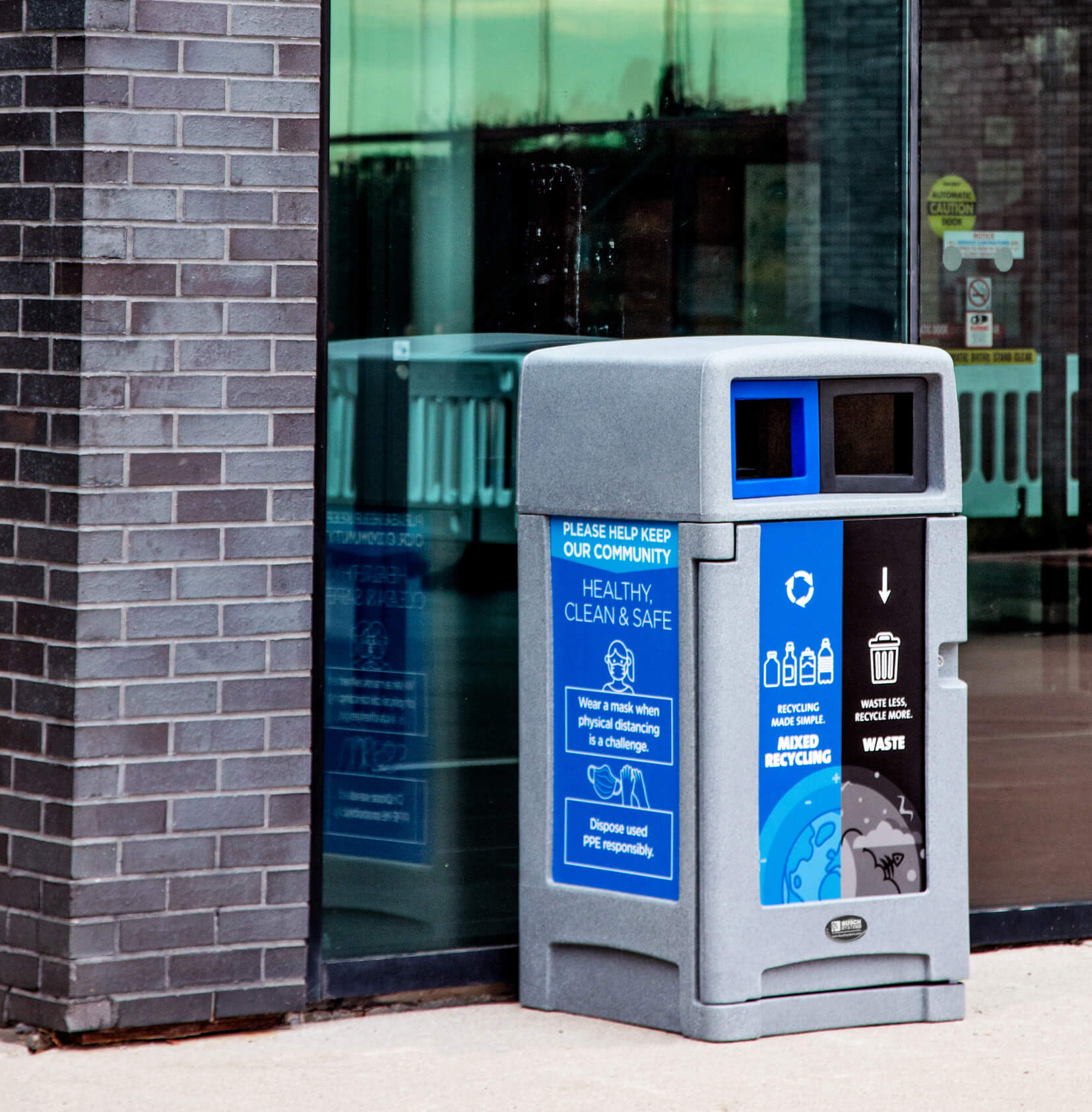 Double exterior waste and recycling container with large signs and restrictive openings in a canopy lid beside a town sports complex
