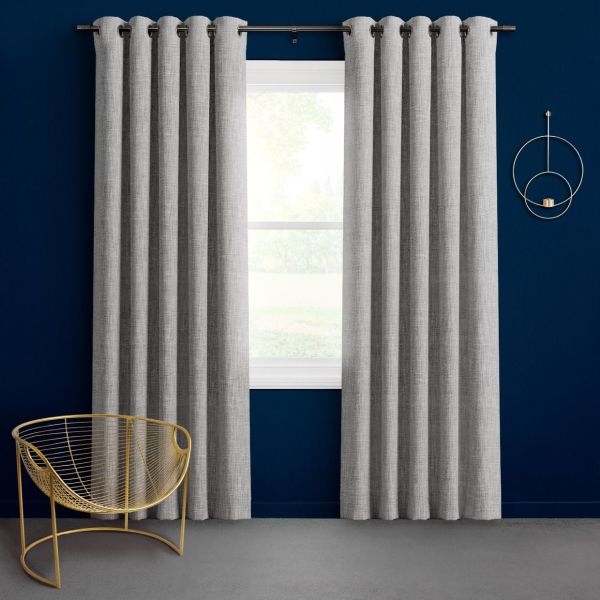 Gray, textured grommet-top curtains, floor-length and evenly pleated, hang on a metal rod flanking a centered window, slightly parted to admit daylight, set against a deep-blue wall with gold accents.