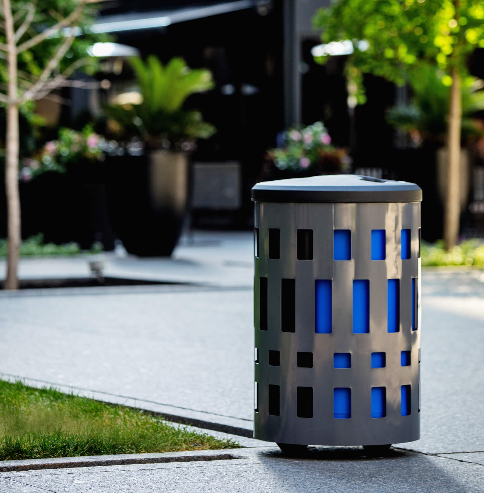 powder coated steel waste and recyclable bin with color liners and black plastic lid outside at a city park