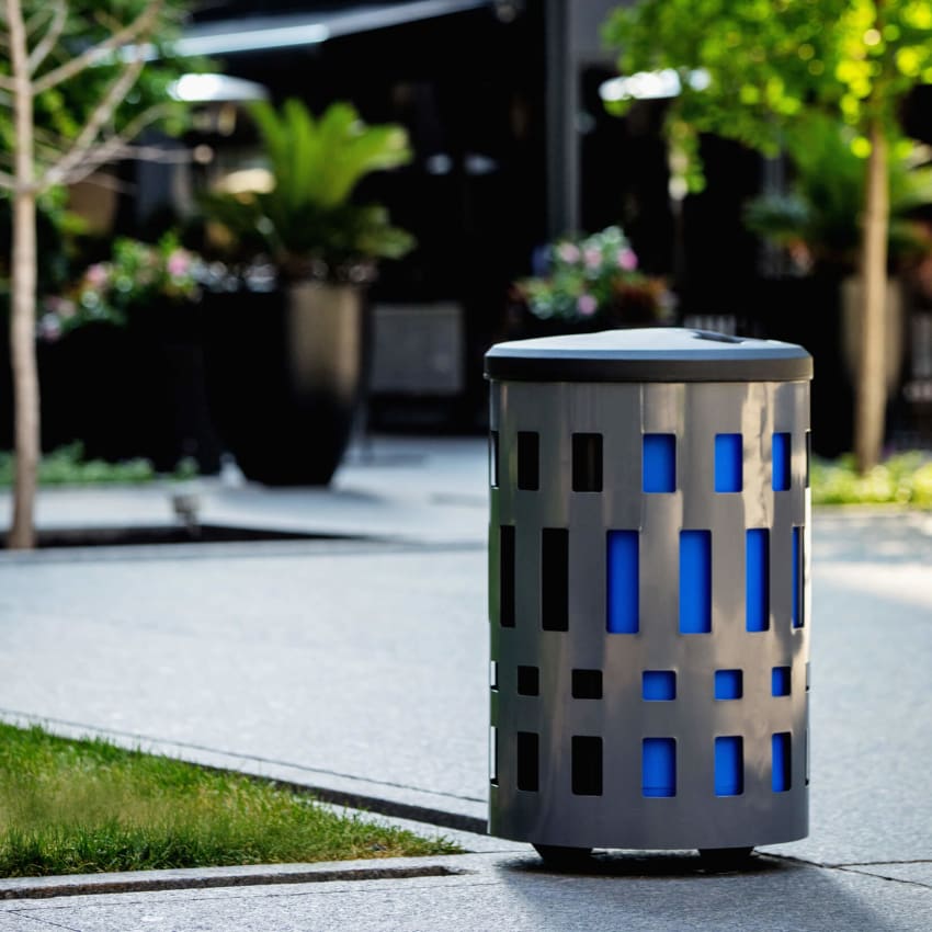 powder coated steel waste and recyclable bin with color liners and black plastic lid outside at a city park