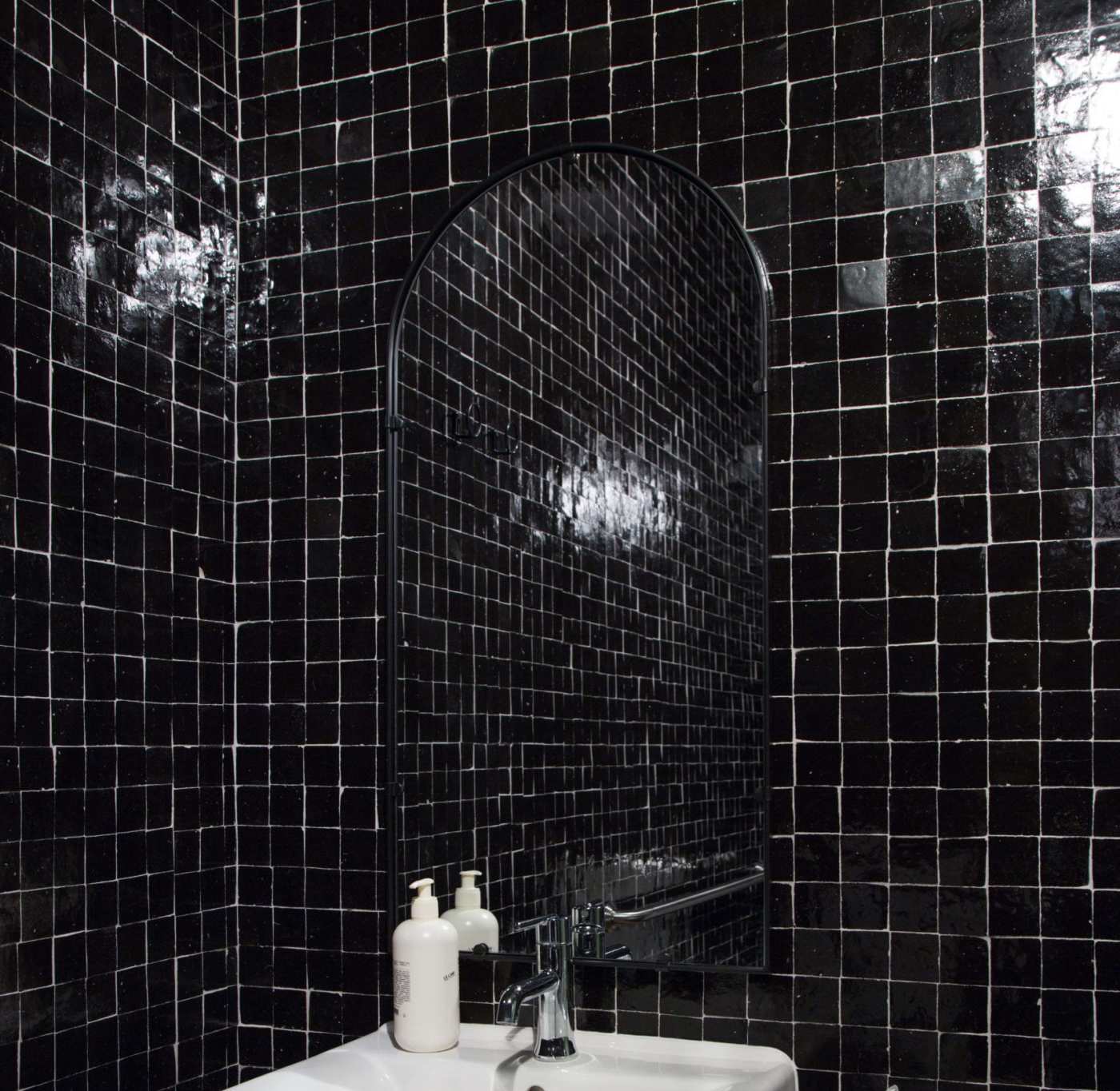 a black tiled bathroom with a sink and mirror.