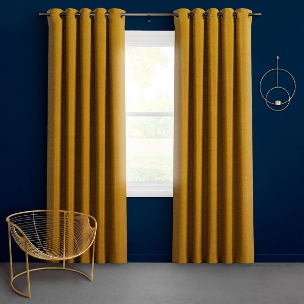 Mustard-gold grommet-top curtains, floor-length on a metal rod, are partially open, filtering bright daylight through a window against a deep navy wall with a gold wire chair and circular sconce.