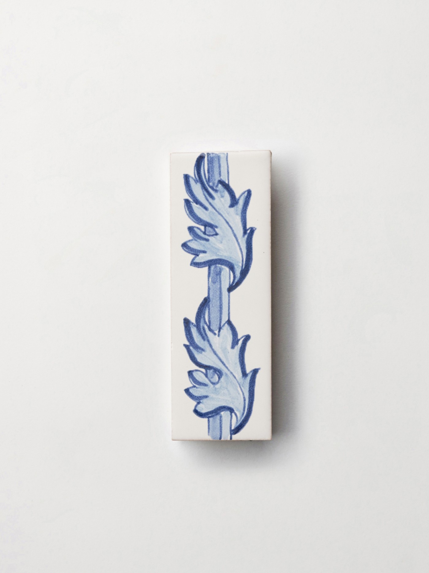 a tile with a white background and two hand painted blue leaves on it.