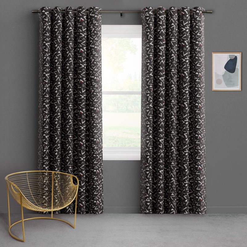 Floor-length charcoal curtains with grommets, white triangle pattern and red accents, pulled aside to reveal a bright window; gray room with a gold wire chair and small abstract framed print.