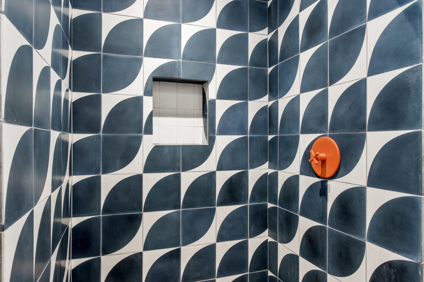 a blue and white tiled shower with an orange knob.