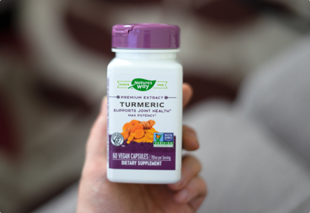 A hand holding a bottle of Turmeric capsules.