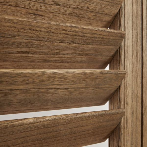 Louvered wooden shutters with wide horizontal slats, angled slightly open, showing pronounced wood grain and beveled edges, close-up interior view with warm tones and light through narrow gaps.
