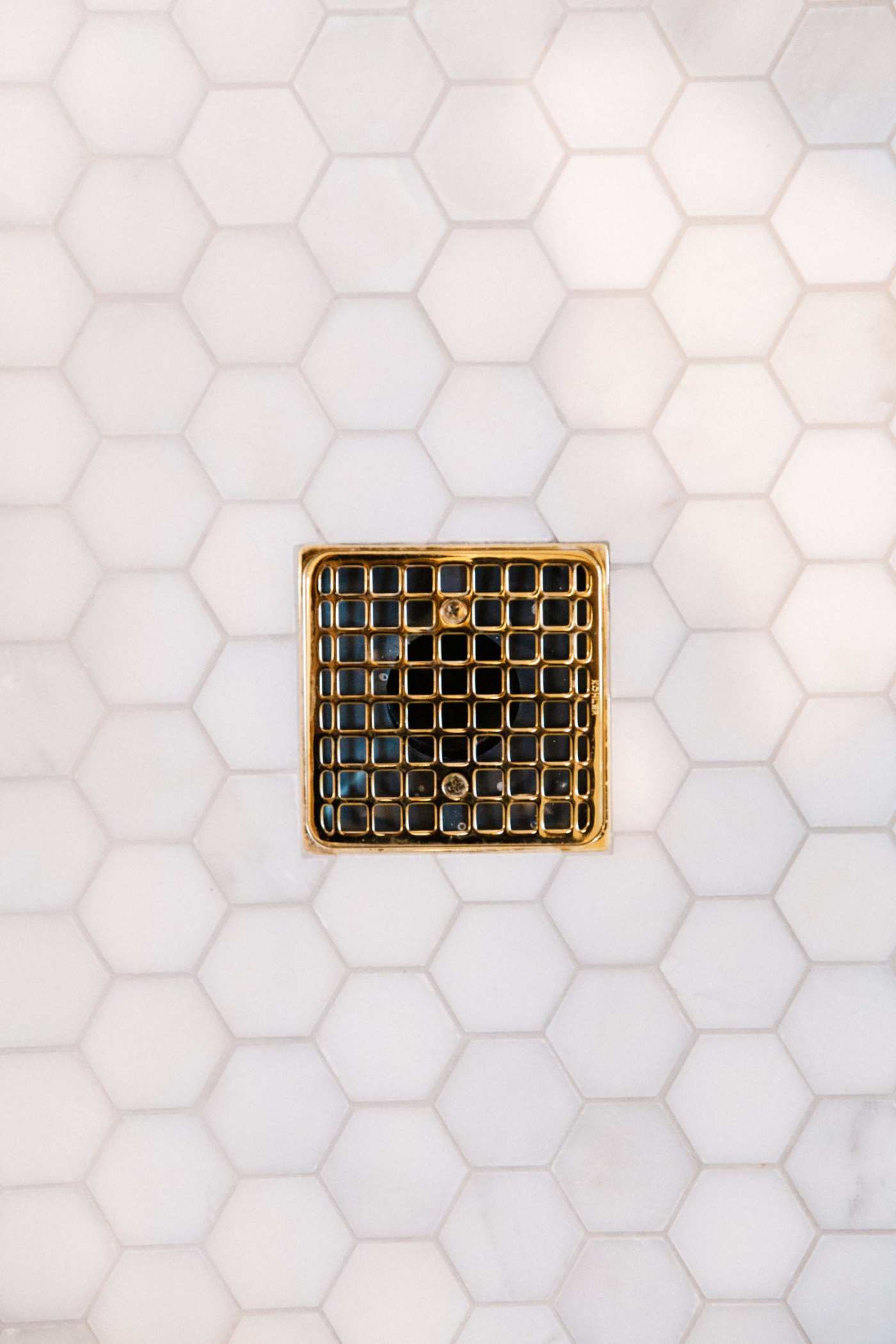 a gold shower drain on a white tiled floor.