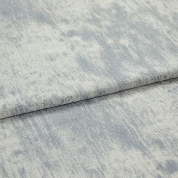 Folded textured fabric with pale blue-gray, mottled brushed pattern; fabric layered in a horizontal fold, lying flat under soft, even studio lighting in a close-up view.