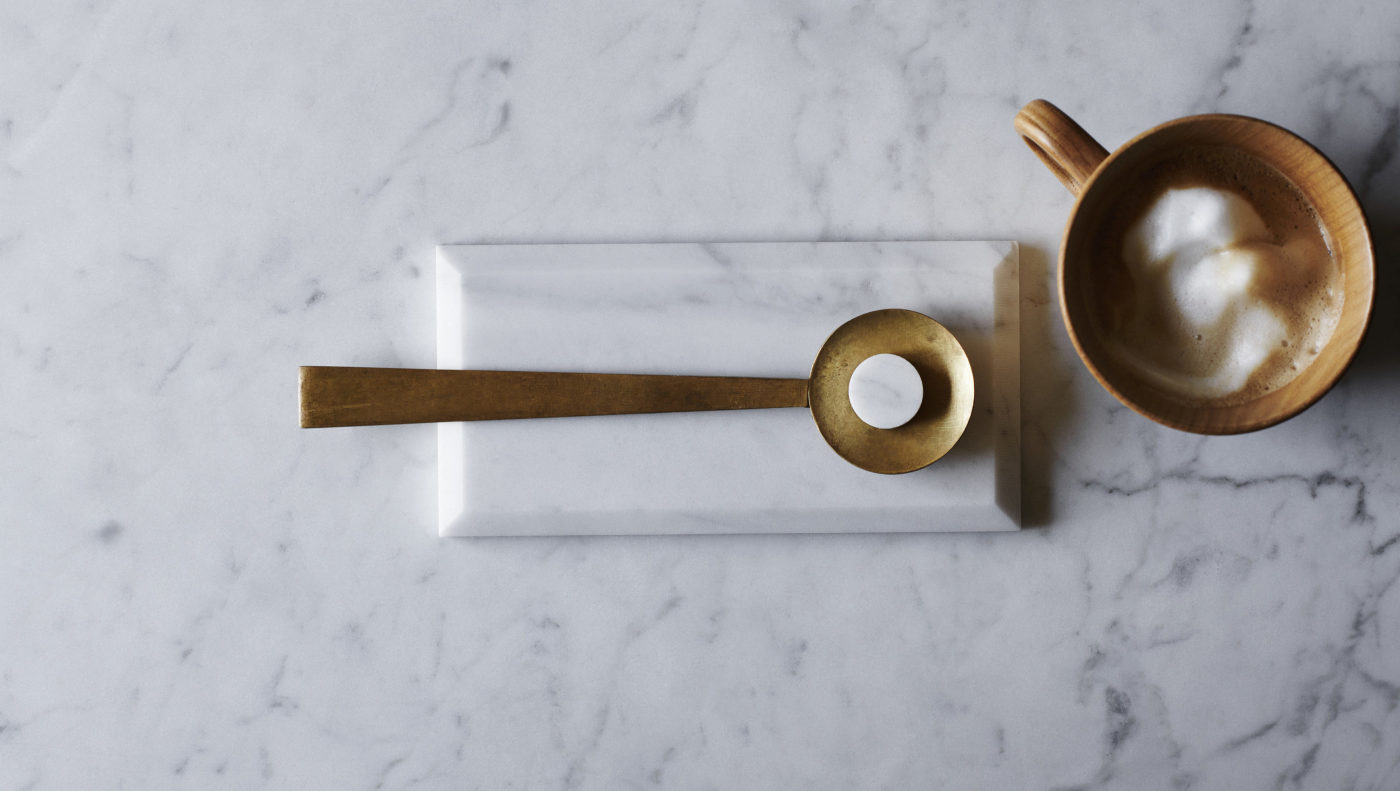 a cup of coffee and a spoon on a white marble countertop.