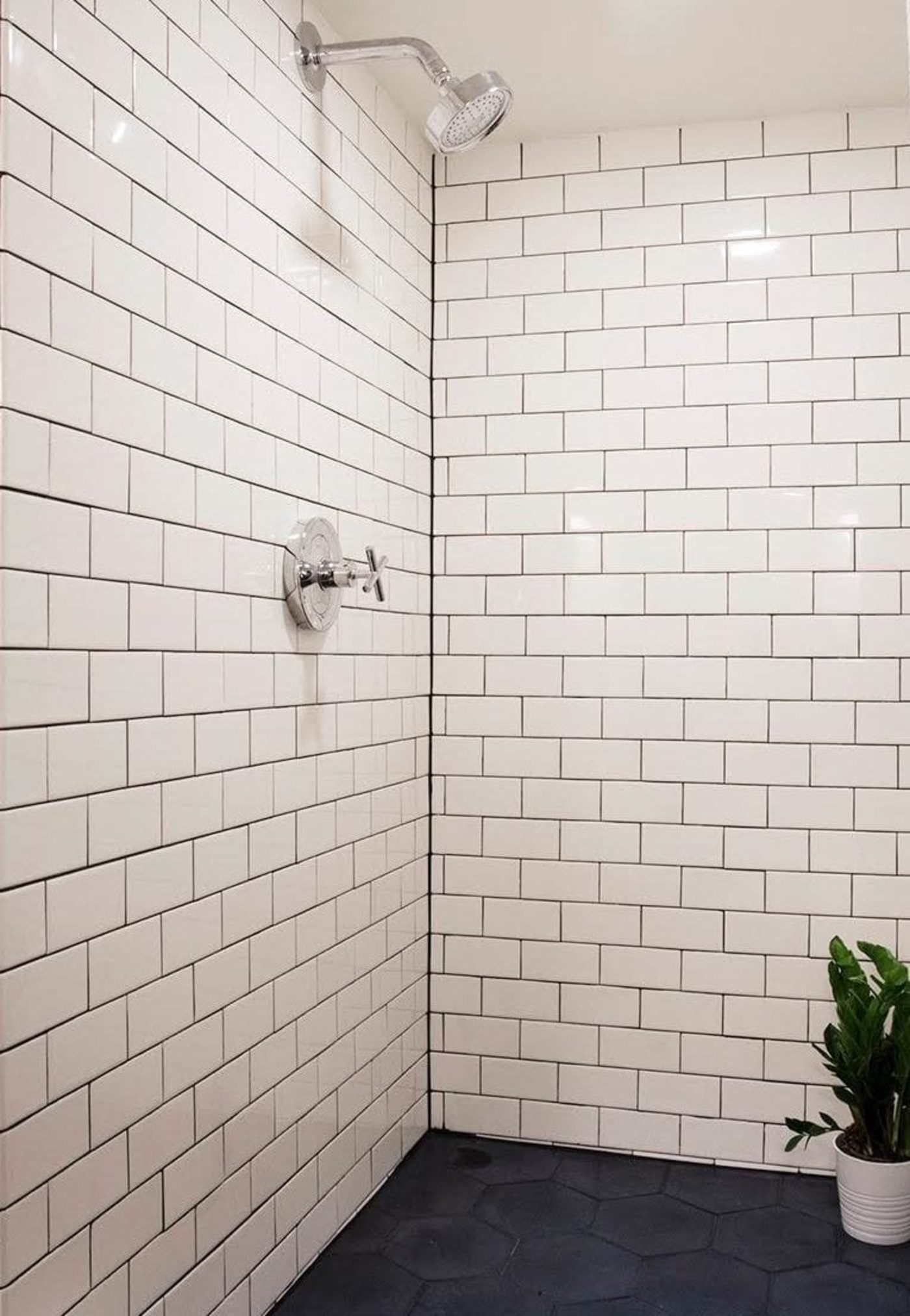 a white tiled shower with a black tiled floor.