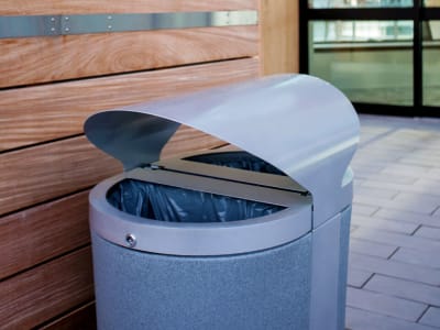 durable powder coated steel outdoor trash and recyclables collection bin with curved metal roof and large capacity liners outside the entrance of a high-end resort