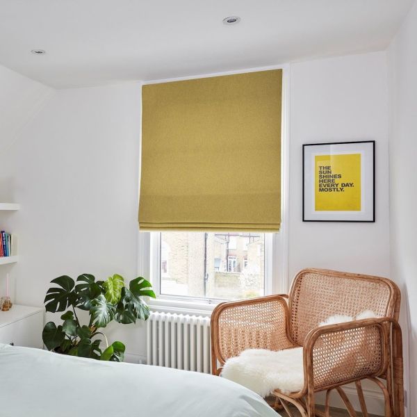 Mustard-yellow Roman blind (lowered, slightly folded at bottom) filtering daylight. Bedroom corner with white walls, rattan armchair topped with sheepskin, monstera plant and a white radiator.

THE SUN SHINES HERE EVERY DAY. MOSTLY.