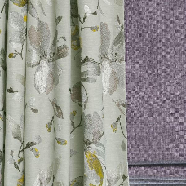 Floral jacquard curtains (left) with soft vertical pleats, hanging and slightly gathered; textured mauve Roman blind (right) folded and lowered; close-up of fabrics in a softly lit interior.