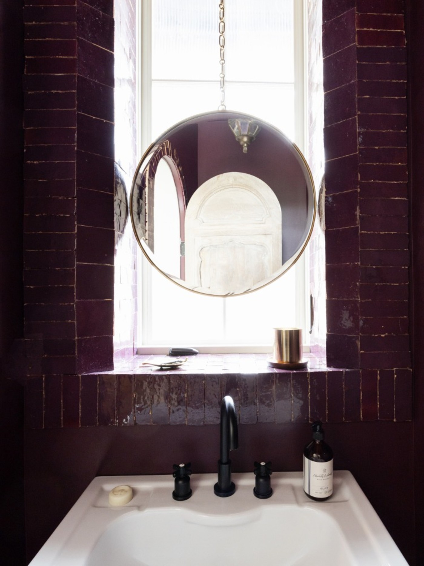 a bathroom with burgundy walls and a round mirror.