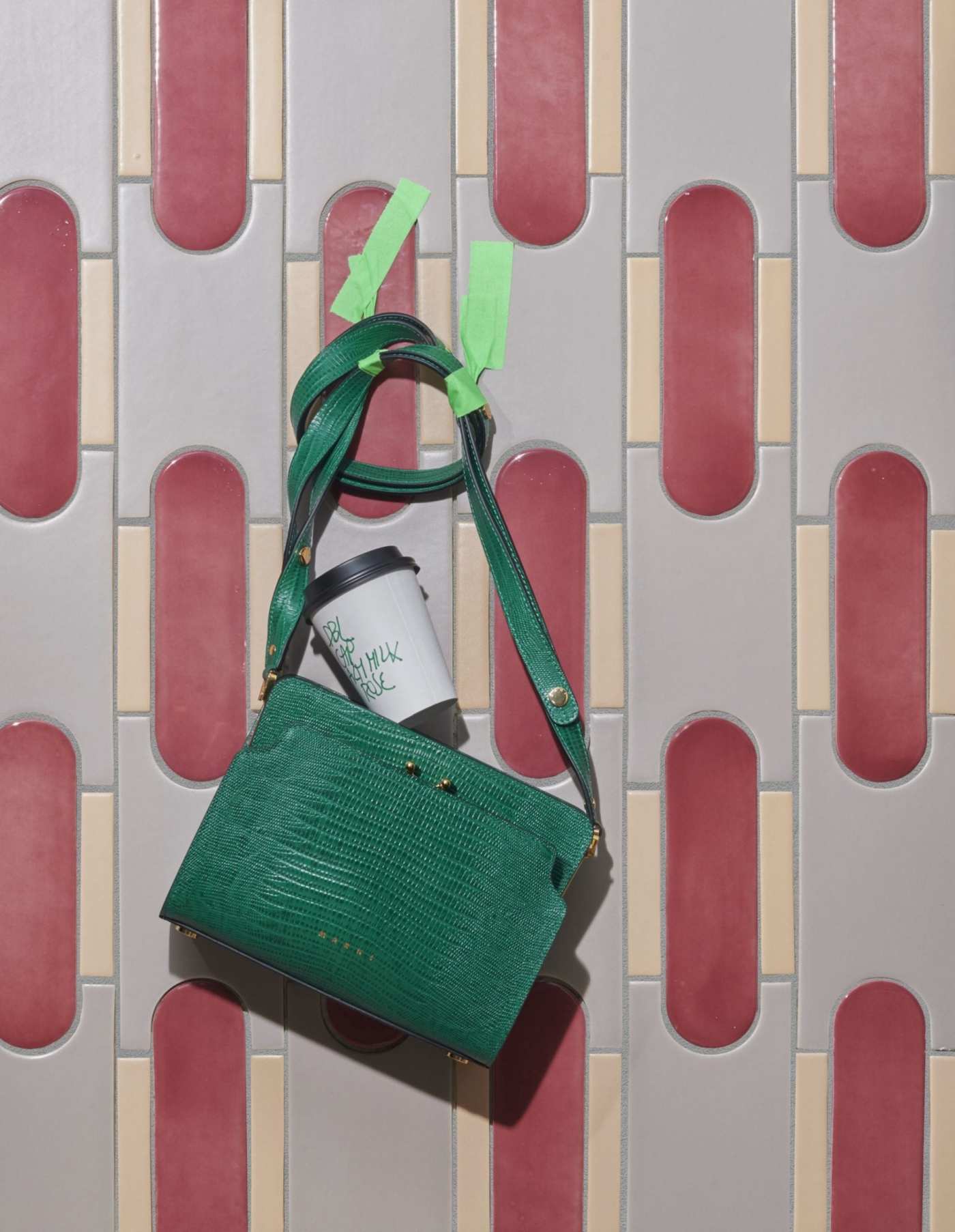 a green handbag on a grey, white, and pink tile surface.