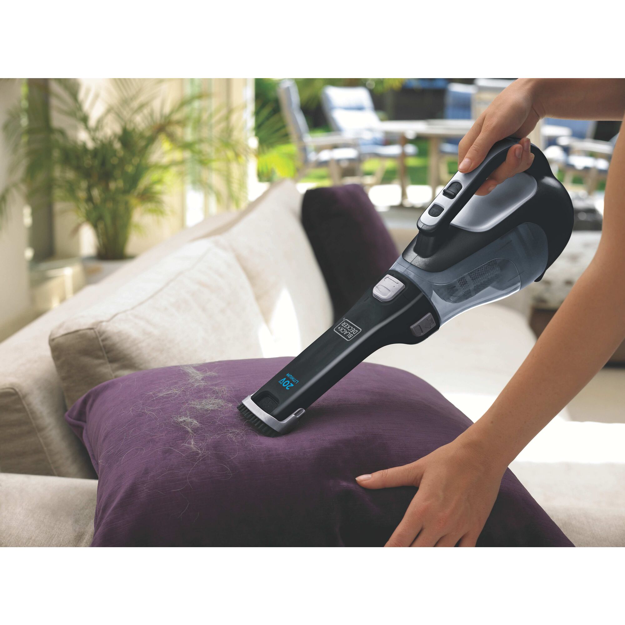 Woman using dustbuster on a sofa vacuuming grey pet hair