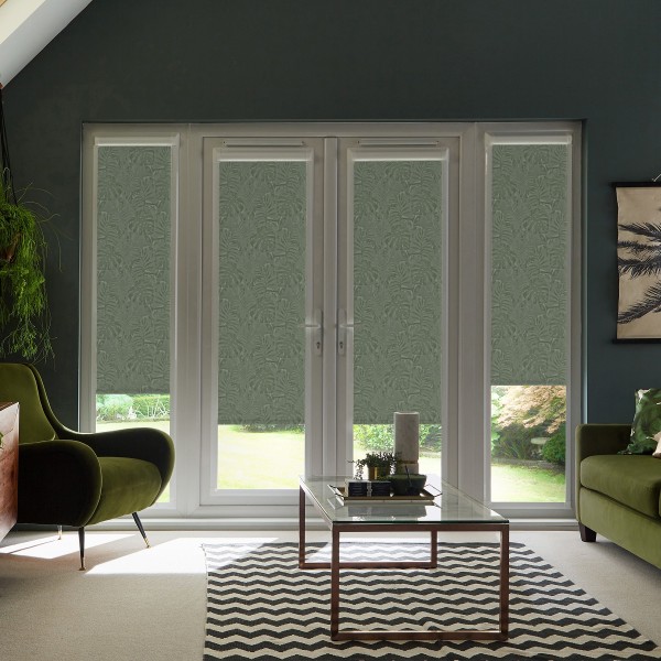 Glass French doors covered by patterned roller blinds that block most light, revealing a garden strip below; modern living room surrounds with green armchairs and a glass coffee table on a chevron rug.