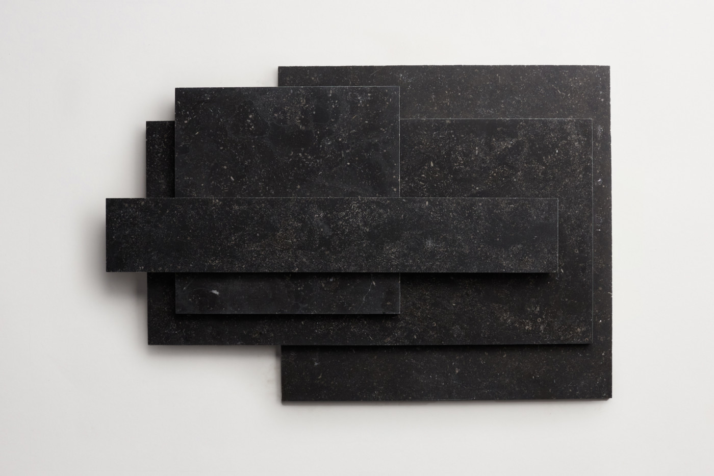 a stack of various sized black limestone tiles on a white surface.