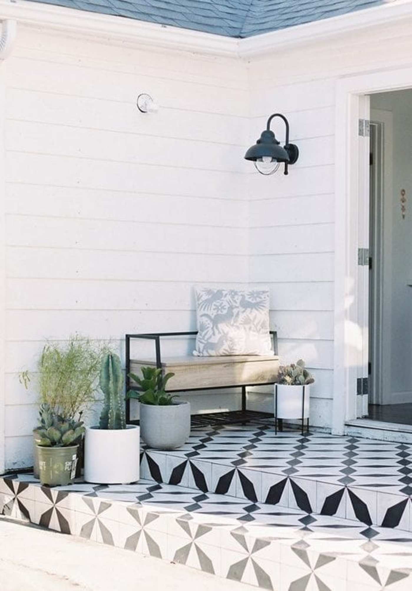 a black and white tiled porch with a potted plant and a bench.