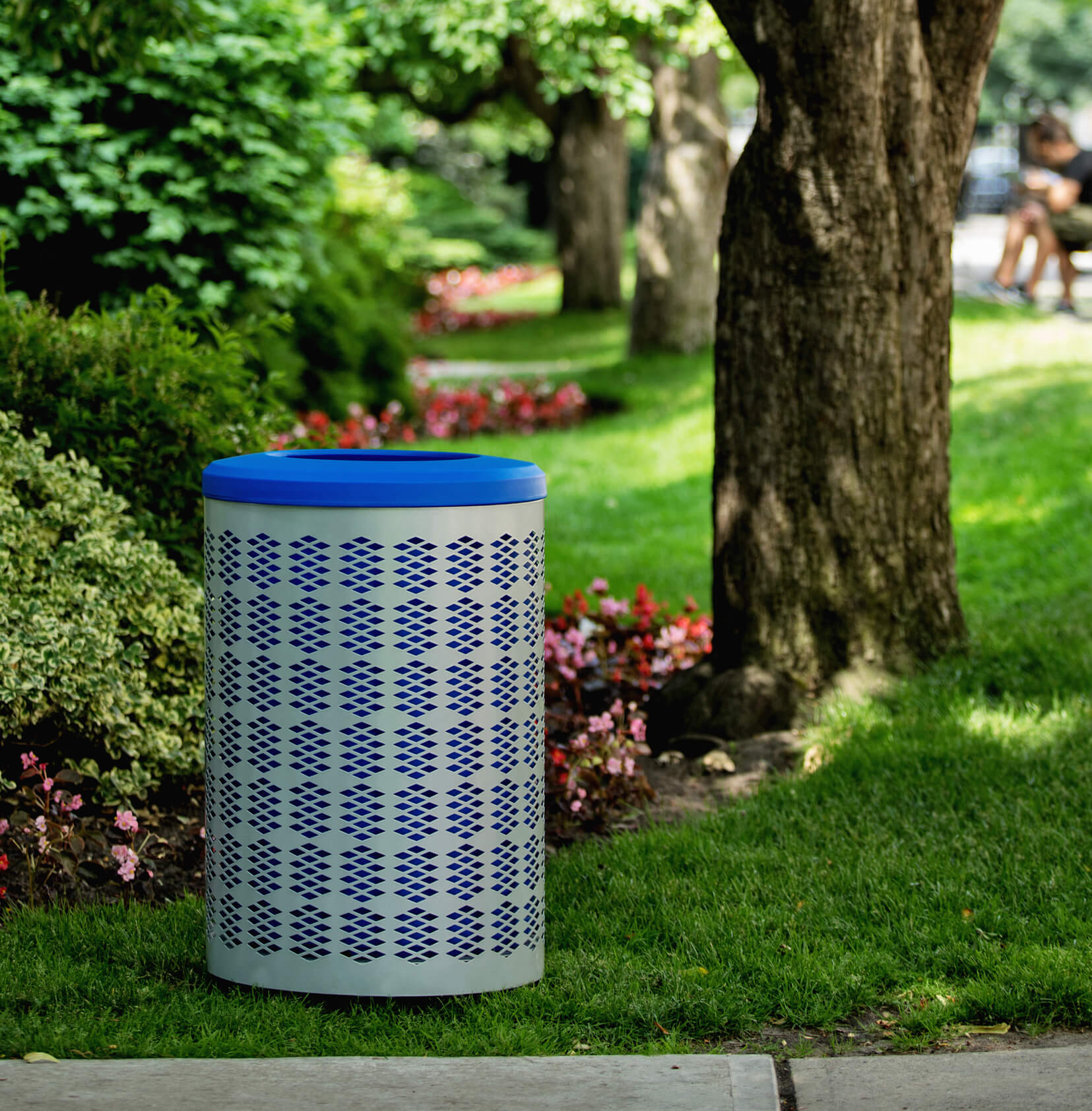 silver powder coated steel recycling bin with a blue liner and blue lid sitting on the grass at a town park area