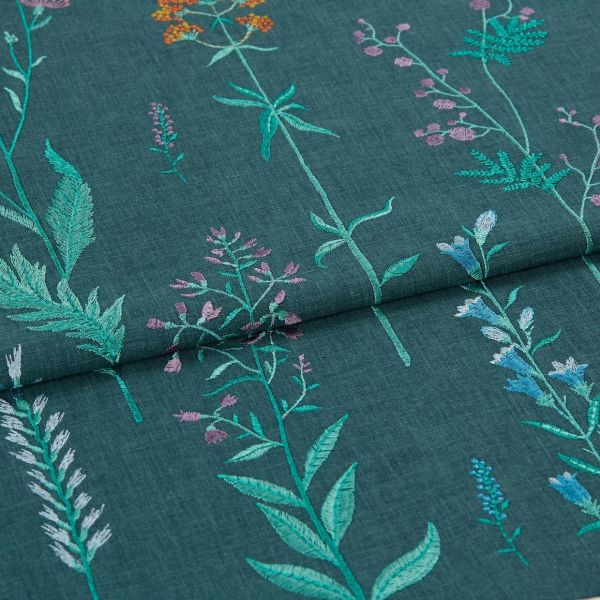 Embroidered teal fabric with vertical stitched wildflower stems — folded once across the middle, showing multicolored threadwork — close-up view with even, soft lighting emphasizing texture.