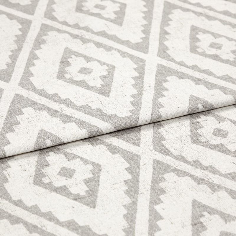 Woven rug with repeating gray diamond-and-zigzag pattern, shown folded once across the center; textured fabric lies flat in soft, even studio lighting, close-up detail view.
