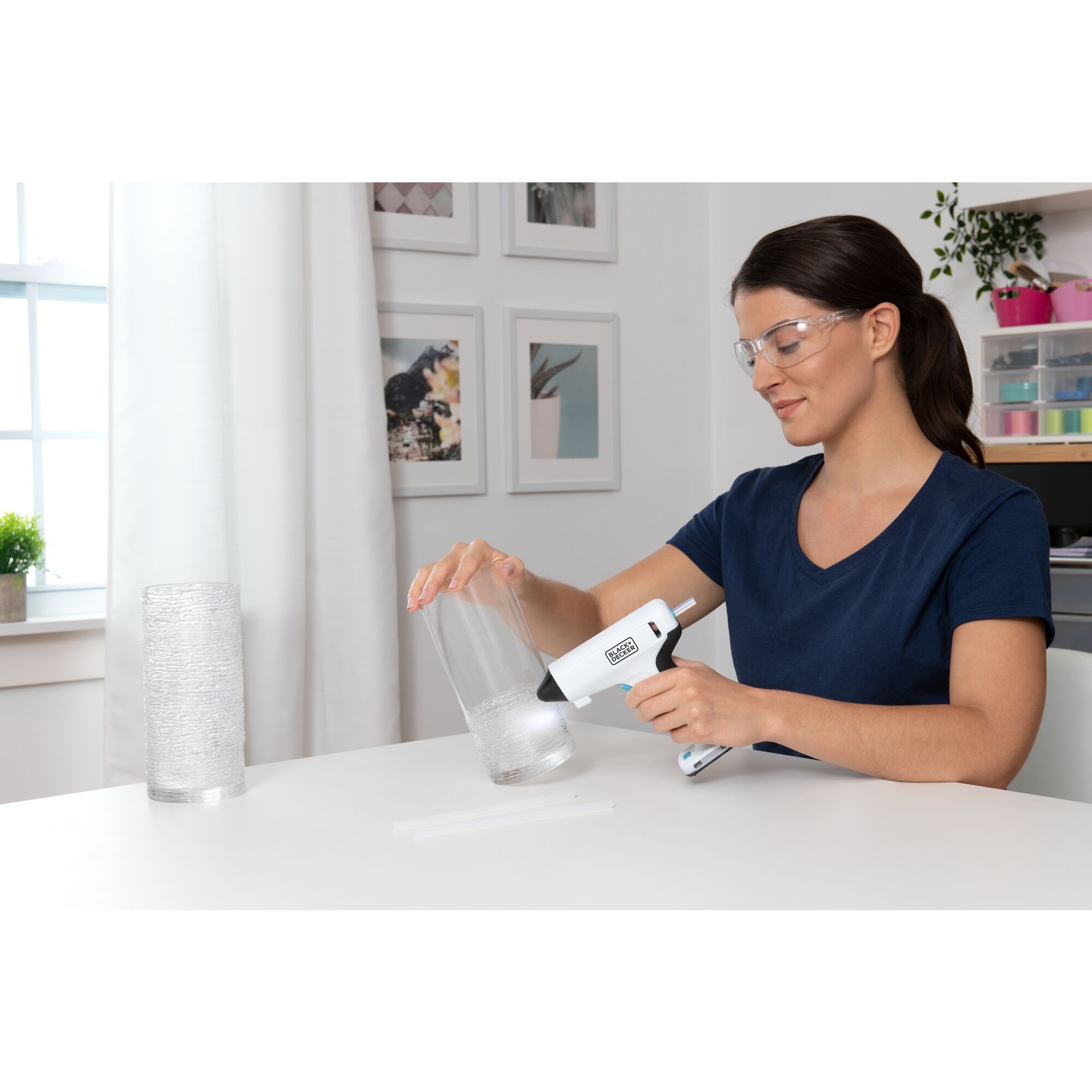 woman sitting in a craft room using a BLACK+DECKER cordless glue gun to decorate a vase