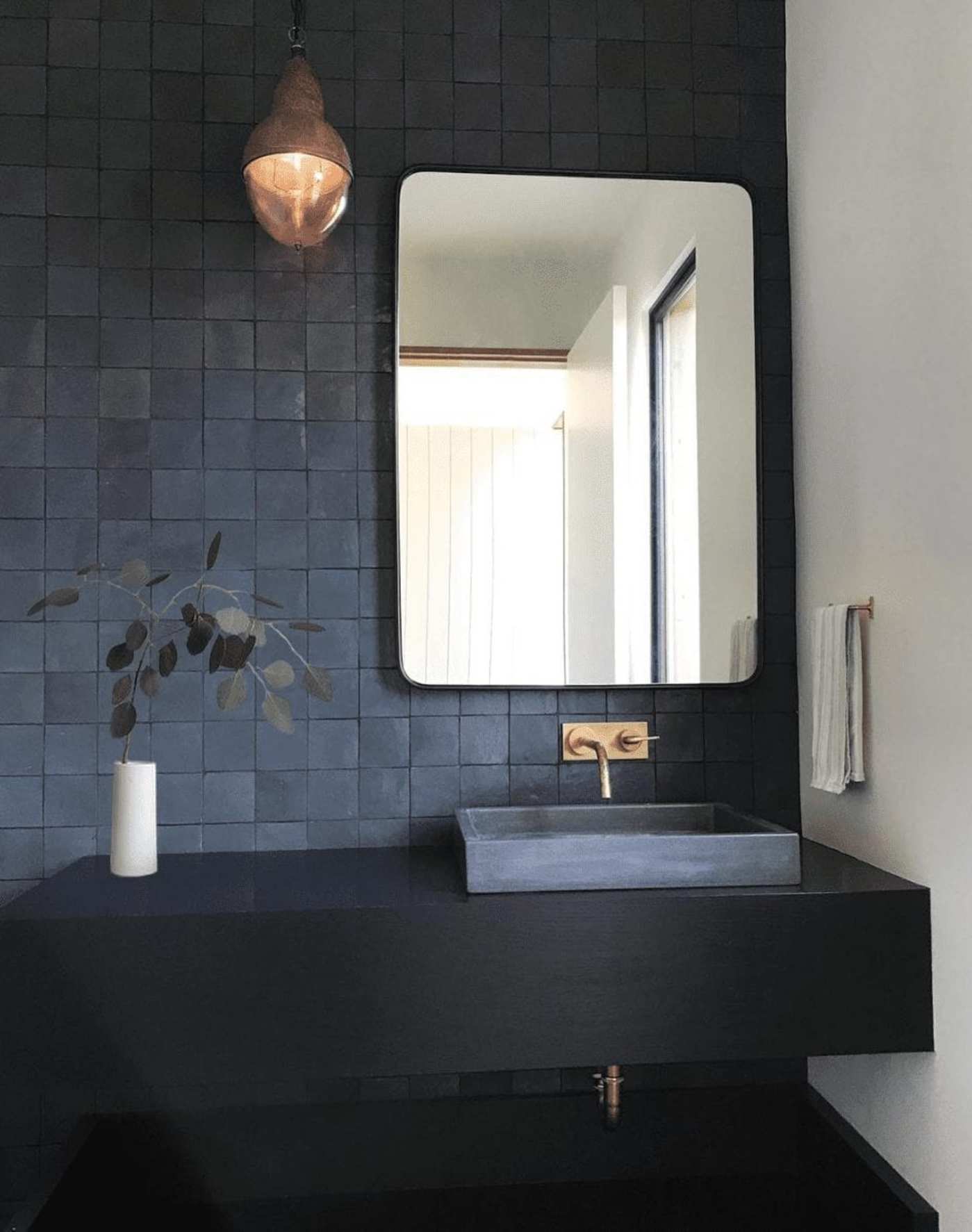 a black tiled bathroom with a sink and mirror.