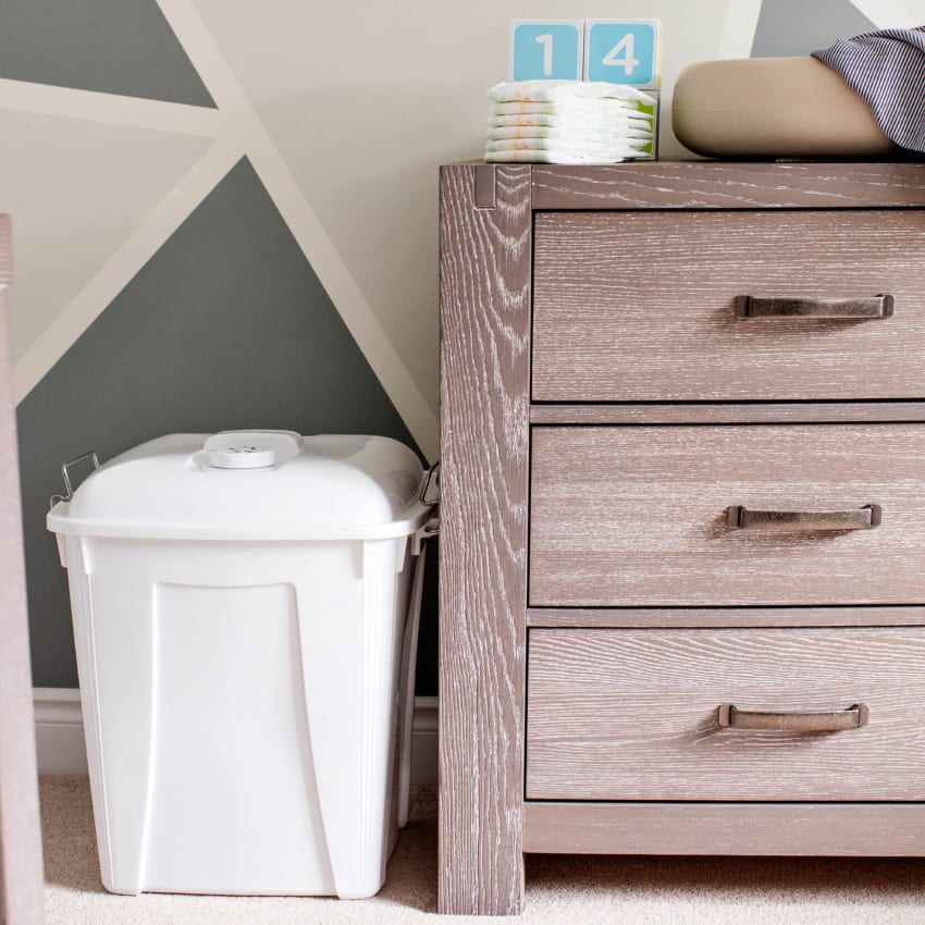 white plastic bin for dirty diapers with a vented lid sitting on the floor in a baby's nursery