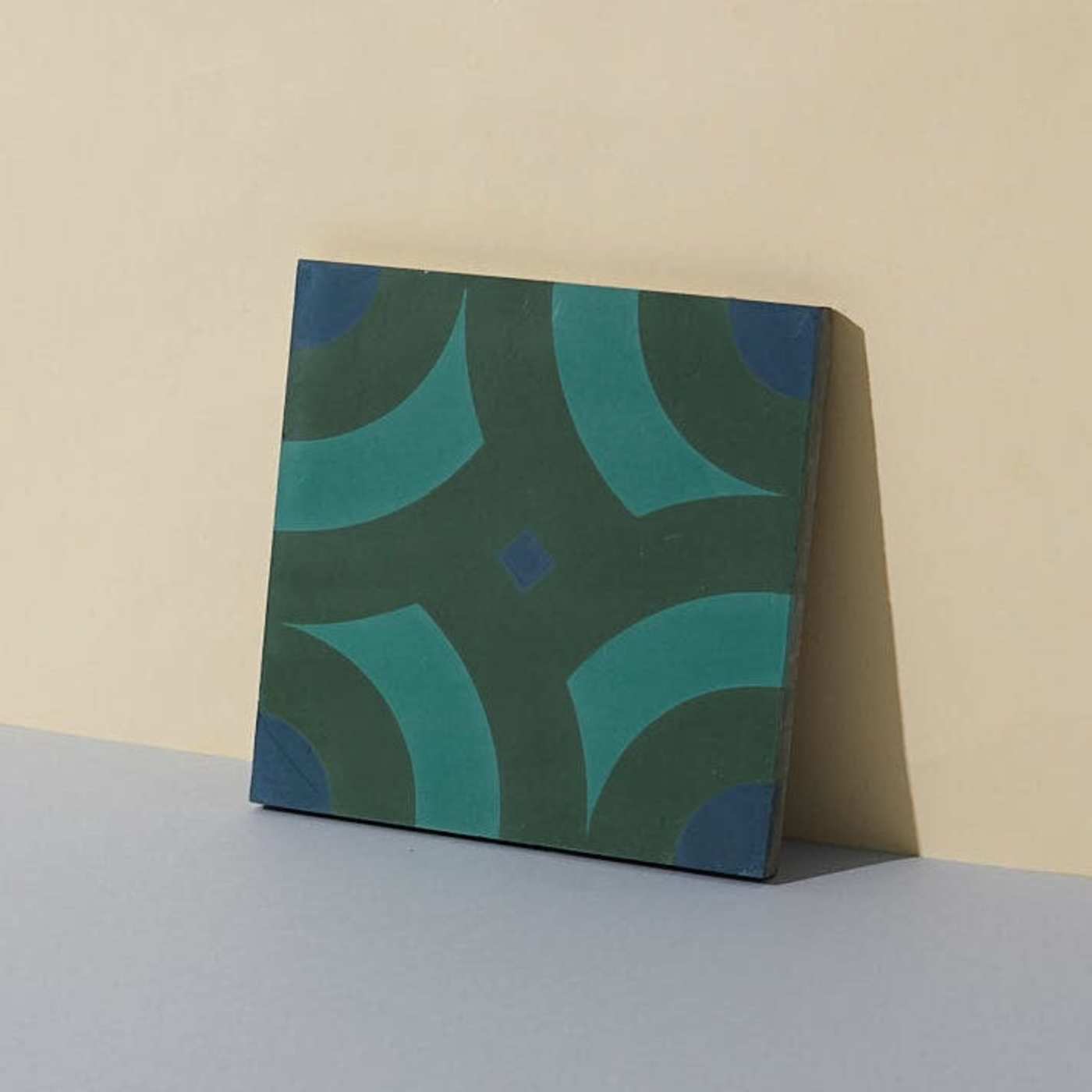 a green and blue tile leaning on a beige wall.