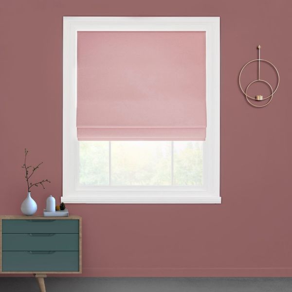 Pink Roman shade, lowered near sill with folds; partially filtering daylight; in a white-trimmed window on a dusty-rose wall above a teal dresser and gold sconce, blurred greenery outside.