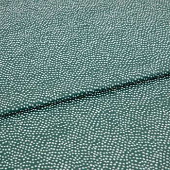 Speckled green fabric (small irregular white dots) folded across center, creating a shallow overlapping crease; close-up on a flat, evenly lit textile sample.