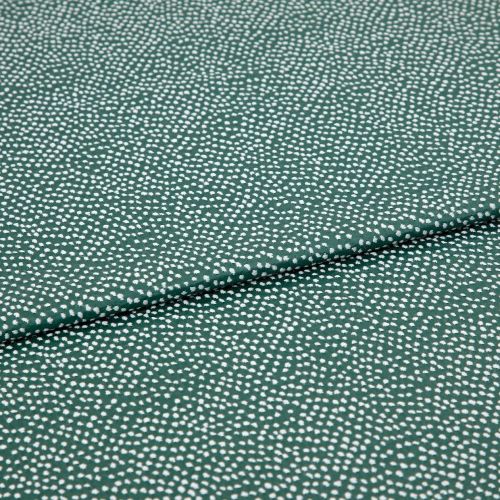 Speckled green fabric (small irregular white dots) folded across center, creating a shallow overlapping crease; close-up on a flat, evenly lit textile sample.