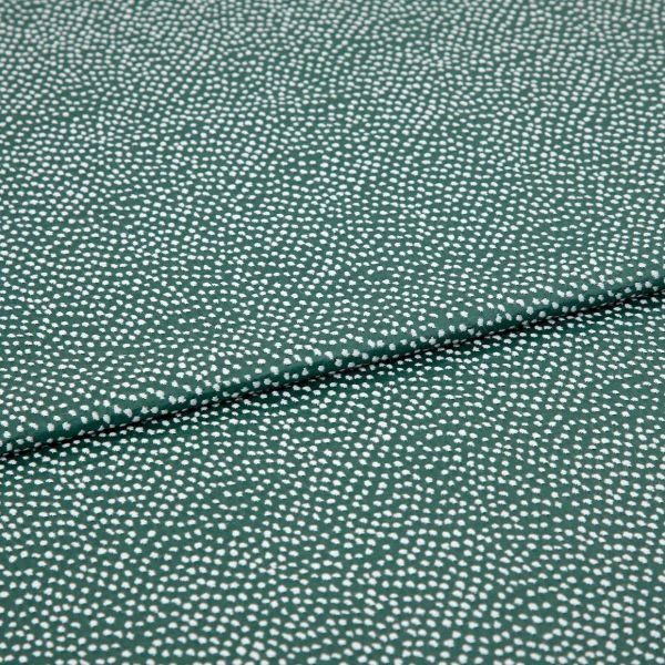 Speckled green fabric (small irregular white dots) folded across center, creating a shallow overlapping crease; close-up on a flat, evenly lit textile sample.