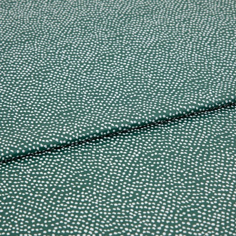 Speckled green fabric (small irregular white dots) folded across center, creating a shallow overlapping crease; close-up on a flat, evenly lit textile sample.