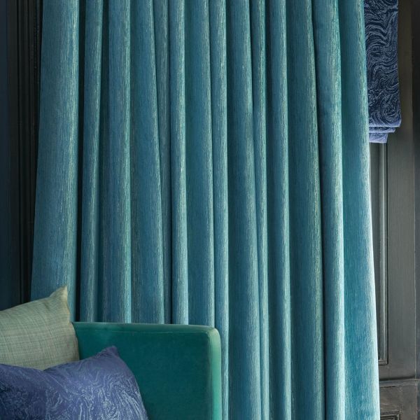 Teal velvet pleated curtains, full-length and subtly shimmering, drawn closed across a window and blocking light; set against dark wood paneling beside a teal sofa with patterned cushions.