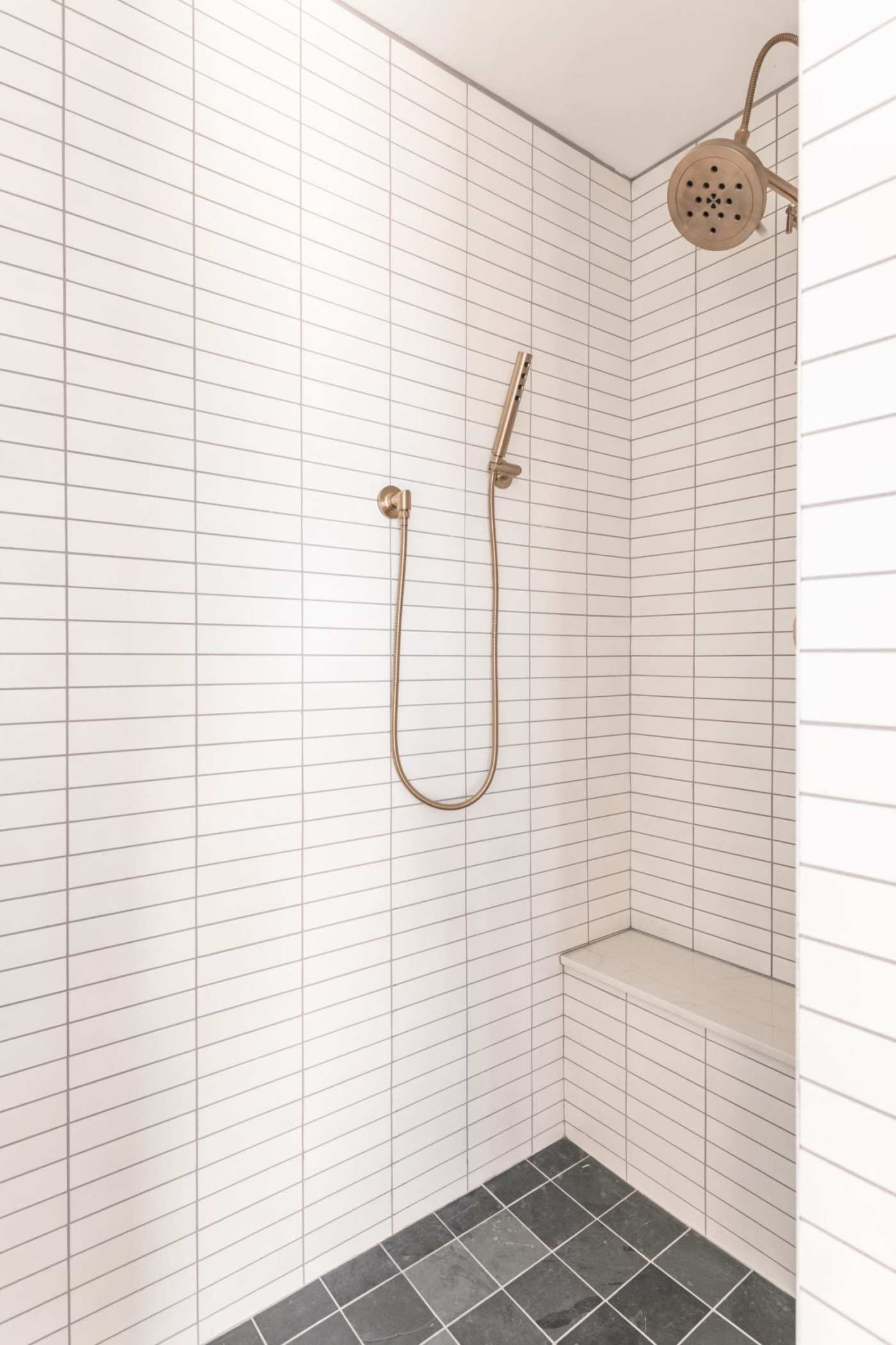 a white tiled shower with a brass shower head.