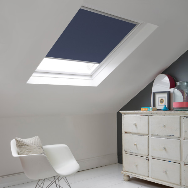 Room with white eaves wall, dark blue-grey wall to right with a shabby chic white drawer unit, a contemporary white chair, white painted floorboards and a skylight blind in oxford blue.