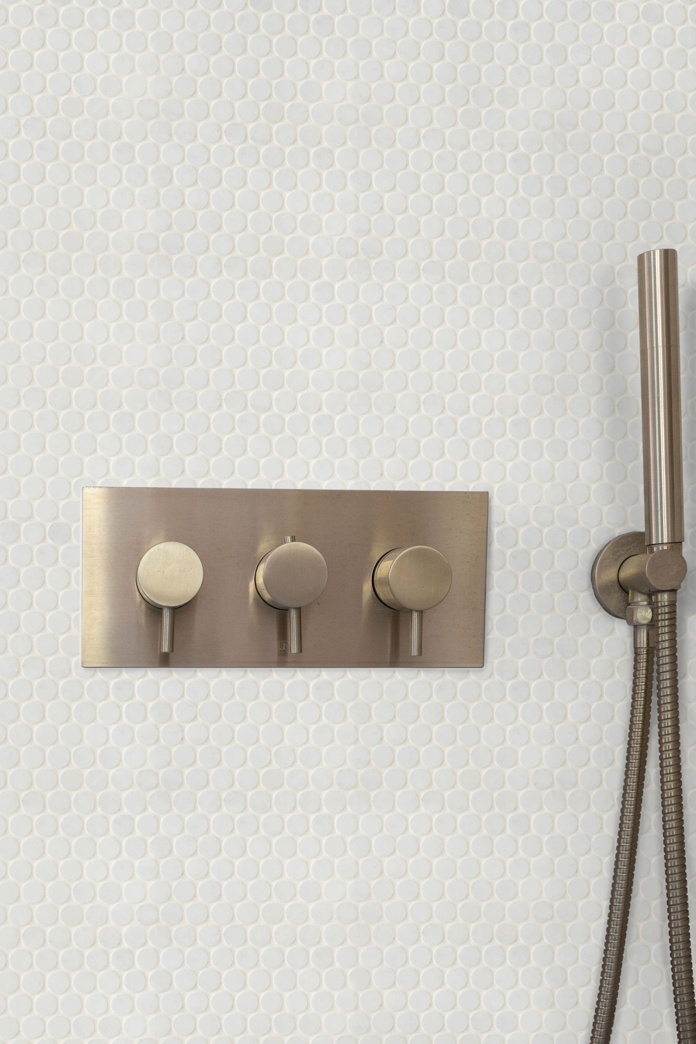 a white tiled shower with grey knobs and a grey showerhead.