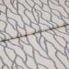 Beige fabric with repeating blue rope-like chain pattern, folded and layered across itself; close-up on a flat surface with soft, even lighting that emphasizes the woven texture.