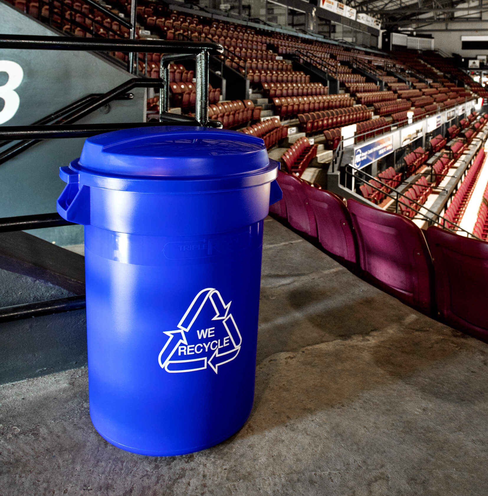 large blue plastic recycling bin with lid and body graphics sitting in a hockey arena