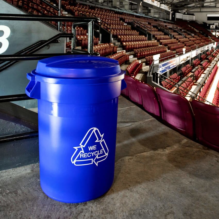 large blue plastic recycling bin with lid and body graphics sitting in a hockey arena