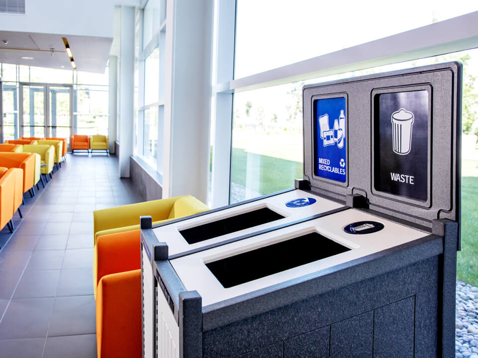 double stream waste and recycling bin with large openings and color-coded signs and labels in the lobby of a modern college campus