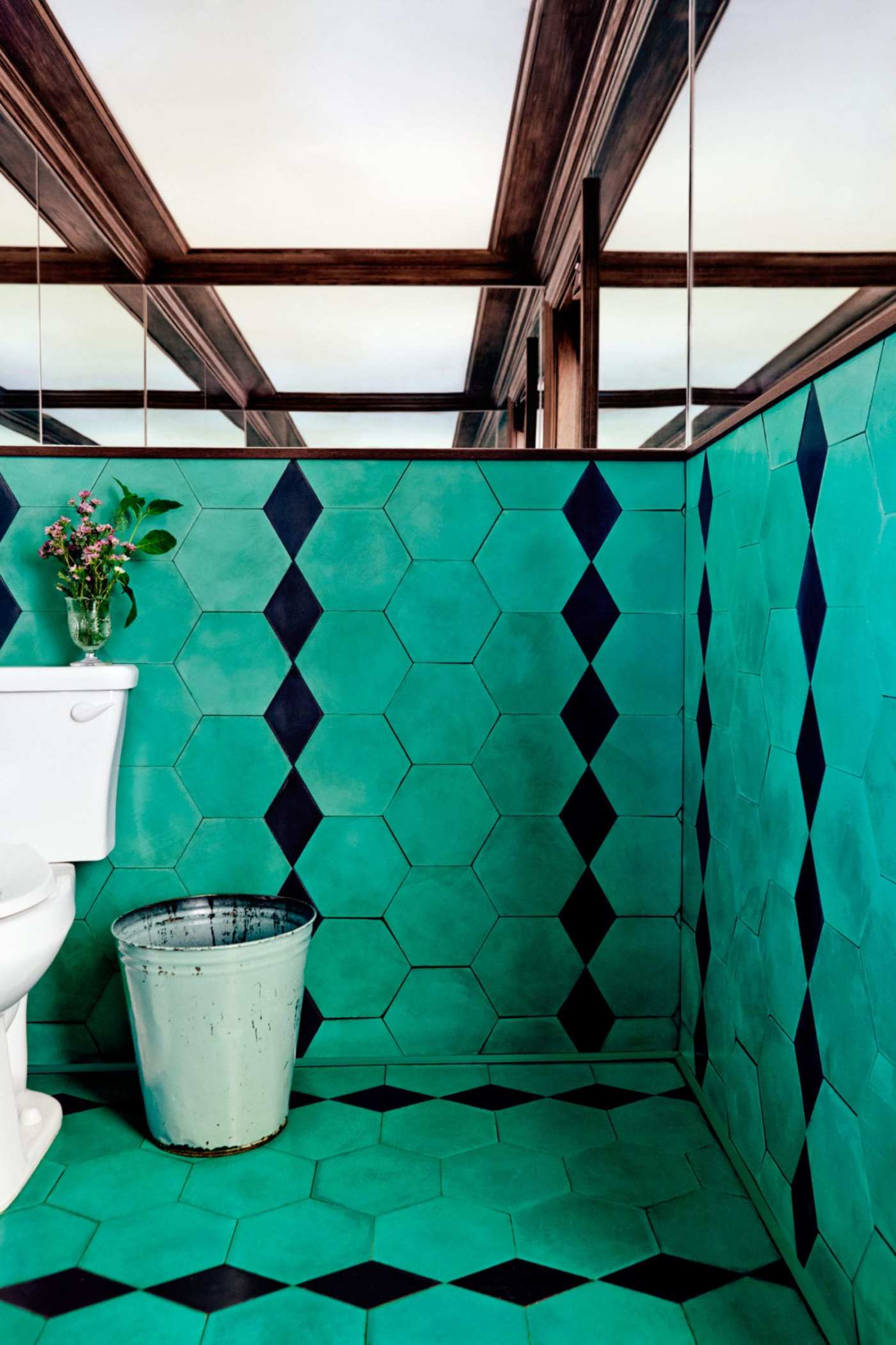 a turquoised tiled bathroom with a toilet and a bucket.