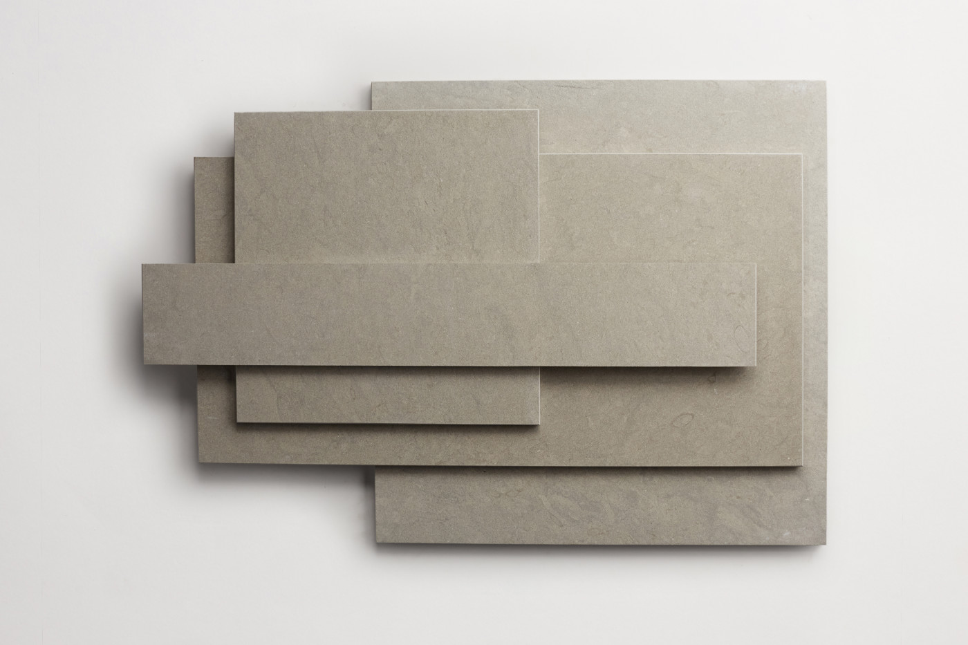 a stack of various sized grey limestone tiles on a white surface.