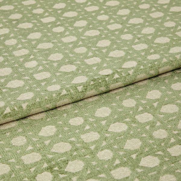 Green patterned woven fabric with raised geometric dots and lattice, folded over itself and showing textured pile; close-up studio view with soft, even lighting emphasizing the fibers.