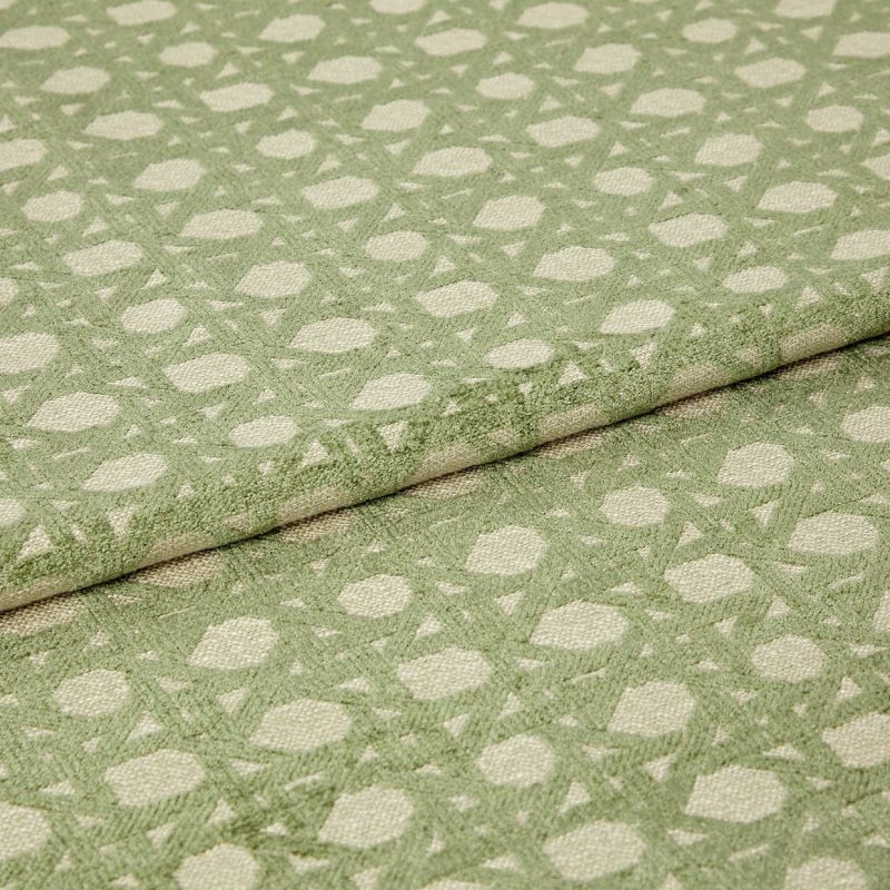 Green patterned woven fabric with raised geometric dots and lattice, folded over itself and showing textured pile; close-up studio view with soft, even lighting emphasizing the fibers.