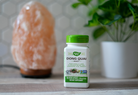 A bottle of Dong Quai Root sitting on a table with a salt lamp and a green plant in the background.