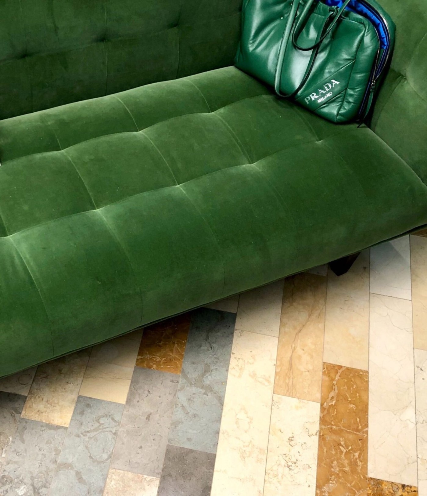 a green couch with a green purse on it standing on a tile floor.